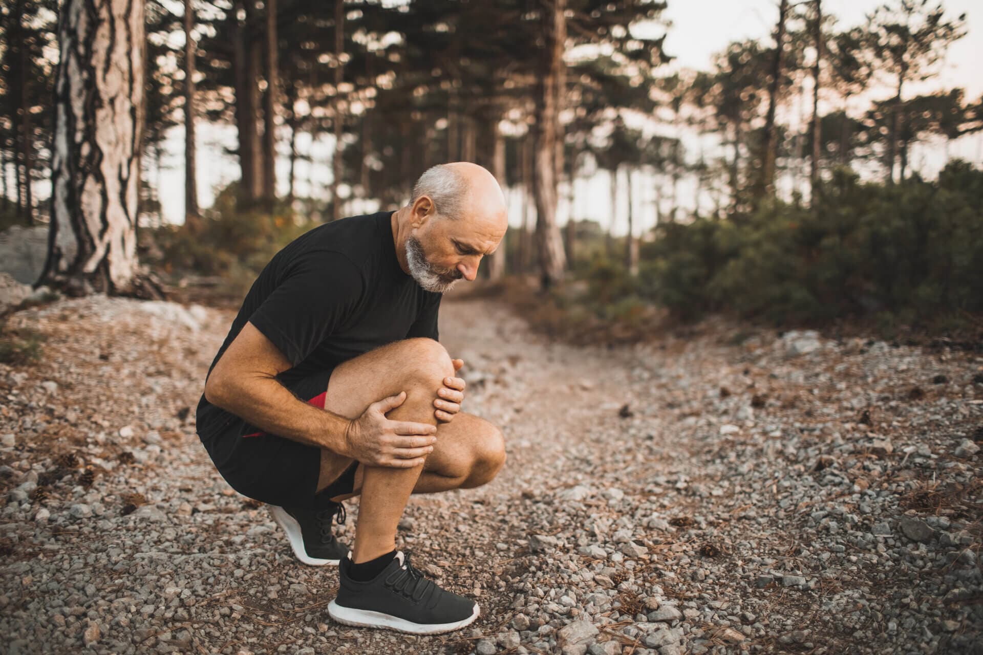 Older man holding his knee whilst on a run in a forest