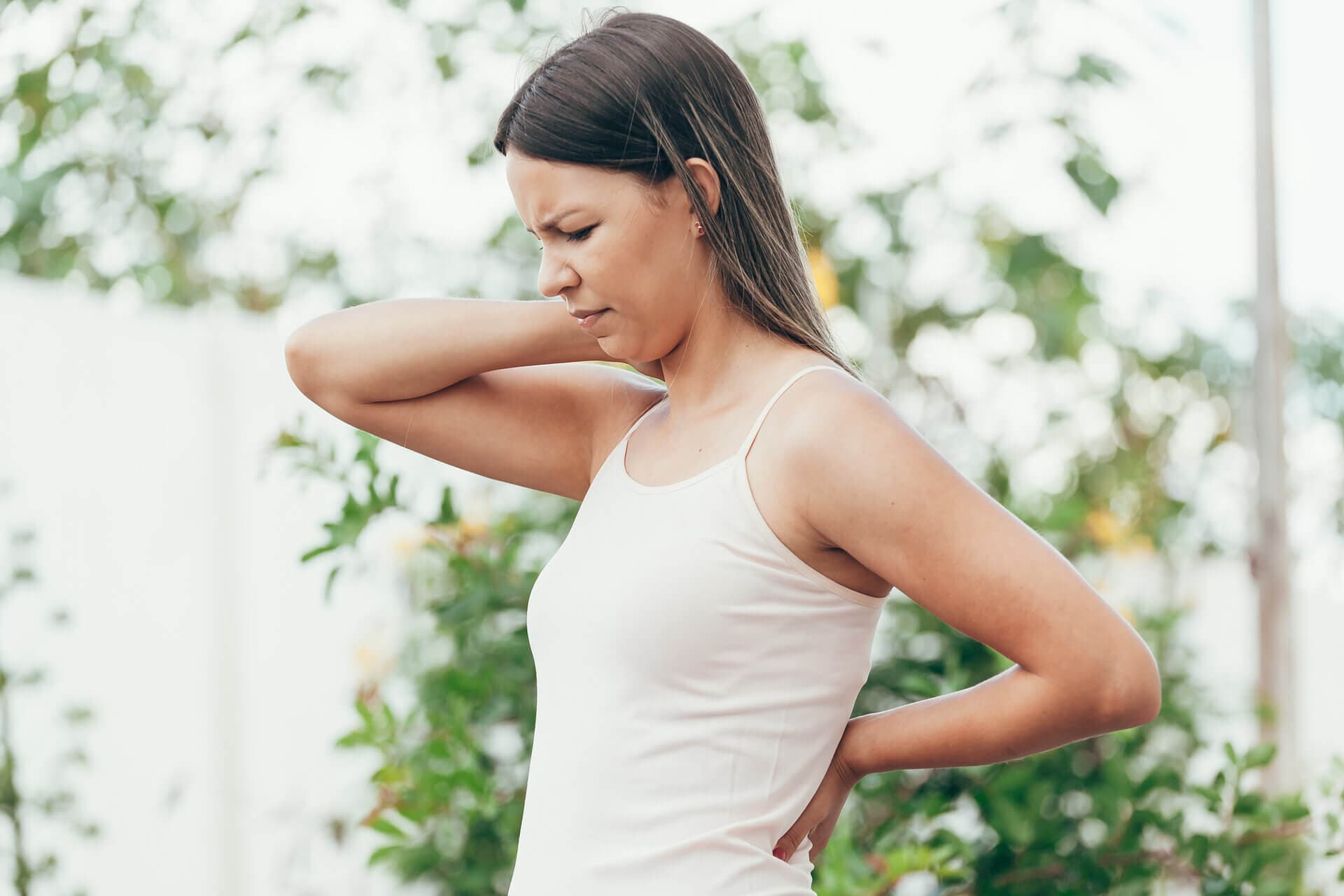 Woman in a park, stopped to hold her back and neck and grimacing